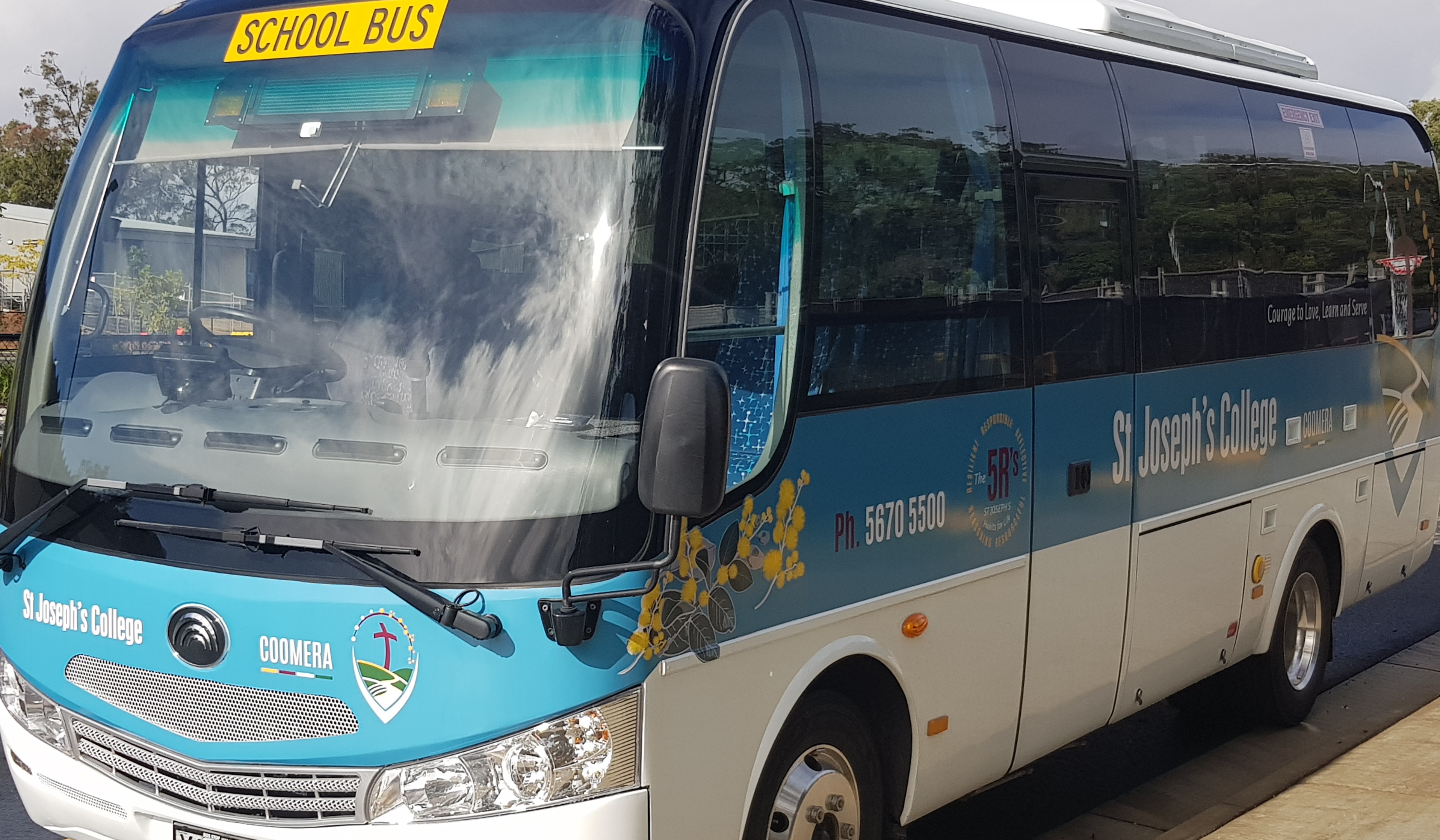 School bus with “School Bus” sign parked outside, branded with St Joseph’s College Coomera logo and contact details on the side.